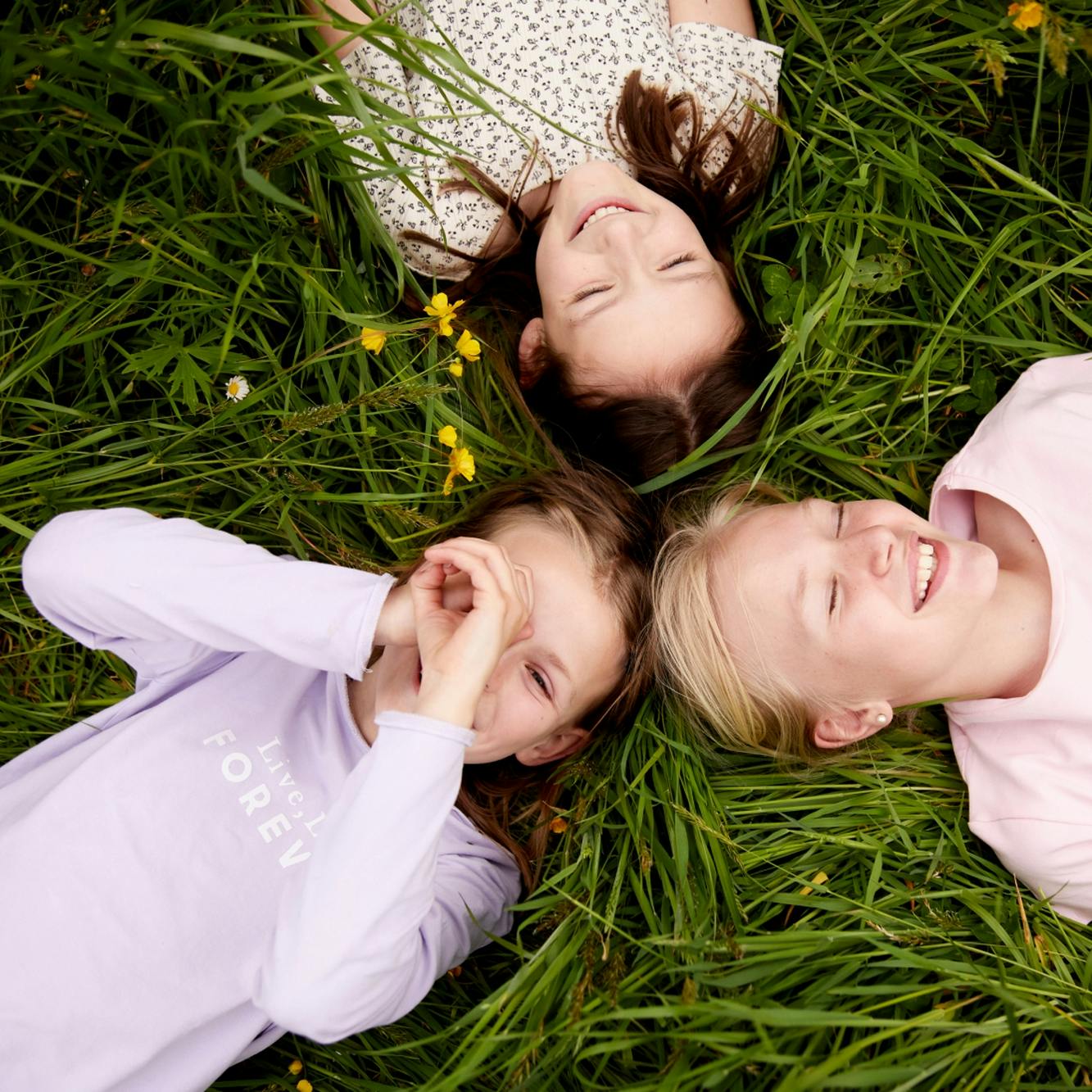 Drei Mädchen liegen in einer Wiese, eine hält die Hände vor das Gesicht wie ein Kaleidoskop © gobiq