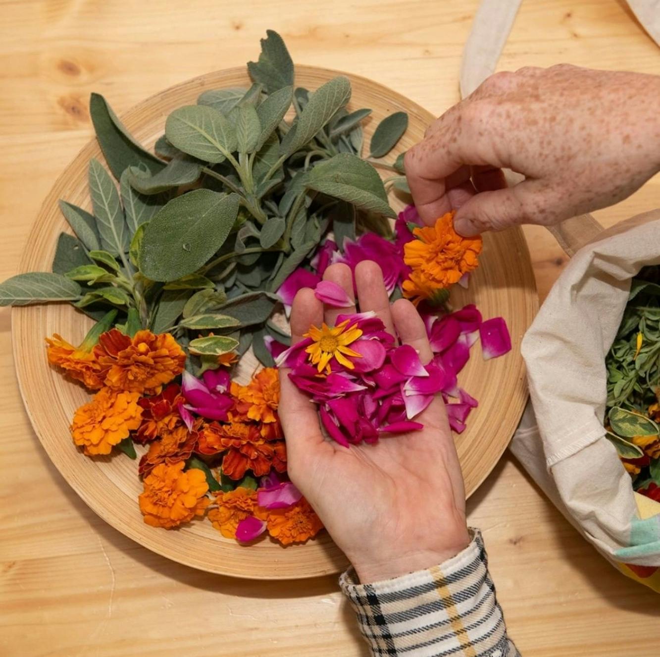 Hände nehmen bunte Blumen und Blätter aus einer Schale © maray festival