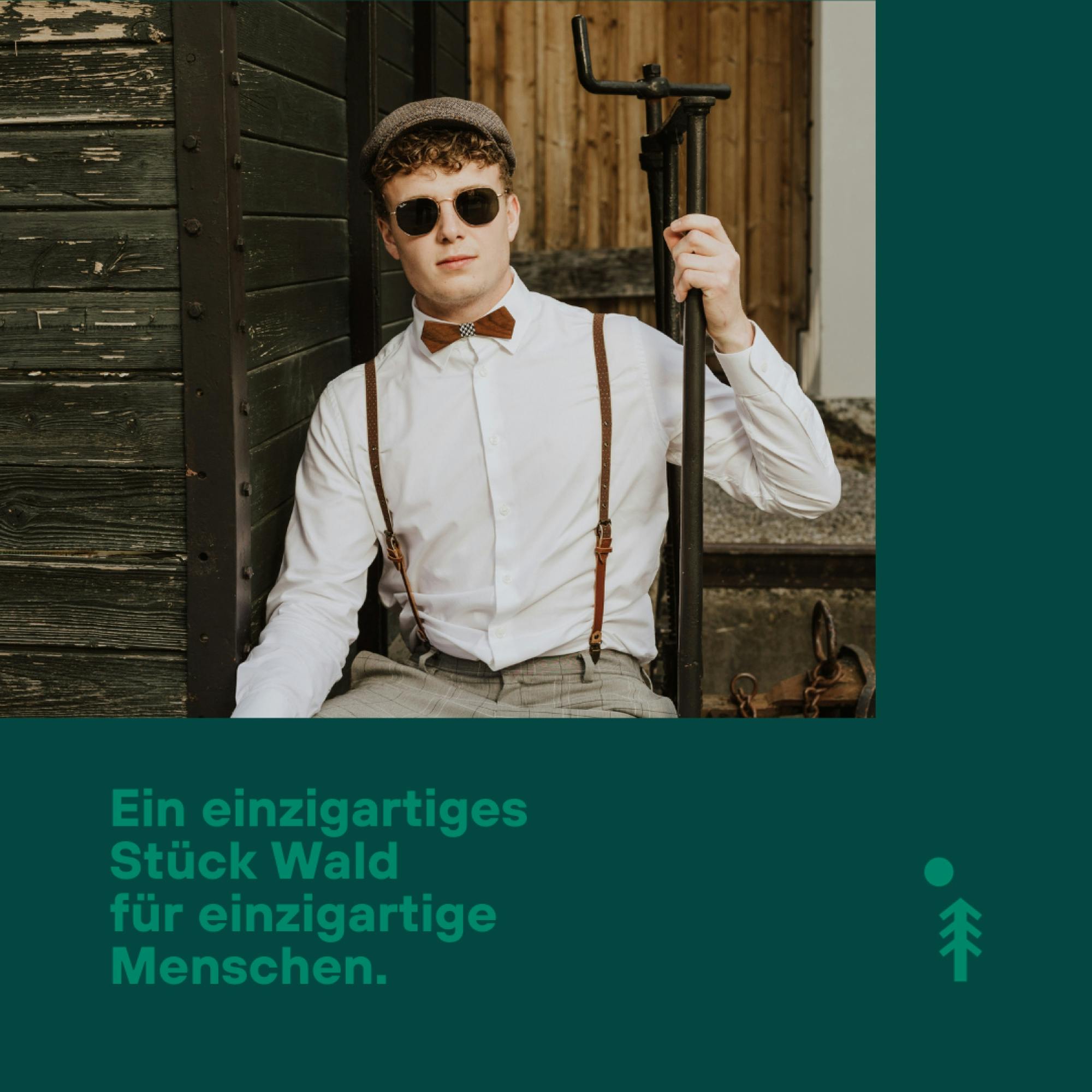 Bild eines jungen stylischen Mannes mit Holzfliege und Hosenträgern auf einem alten Zugwagon mit dem Textinsert: Ein einzigartiges Stück Wald für einzigartige Menschen © good matters
