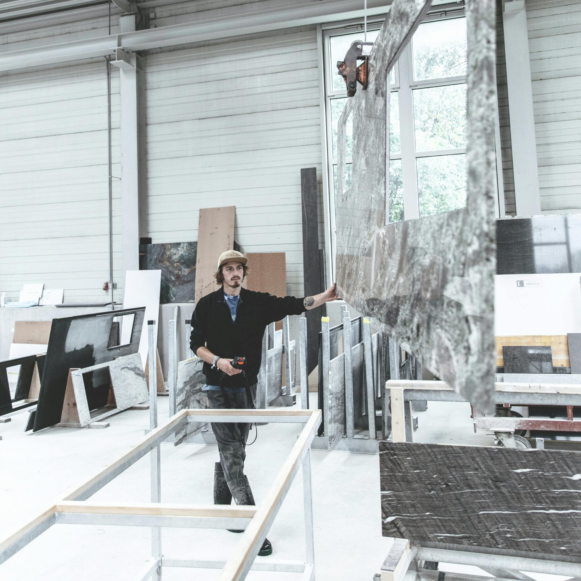 Ein Mitarbeiter hebt in der Werkstatt mit einem Kran eine Arbeitsplatte hoch. © gobiq