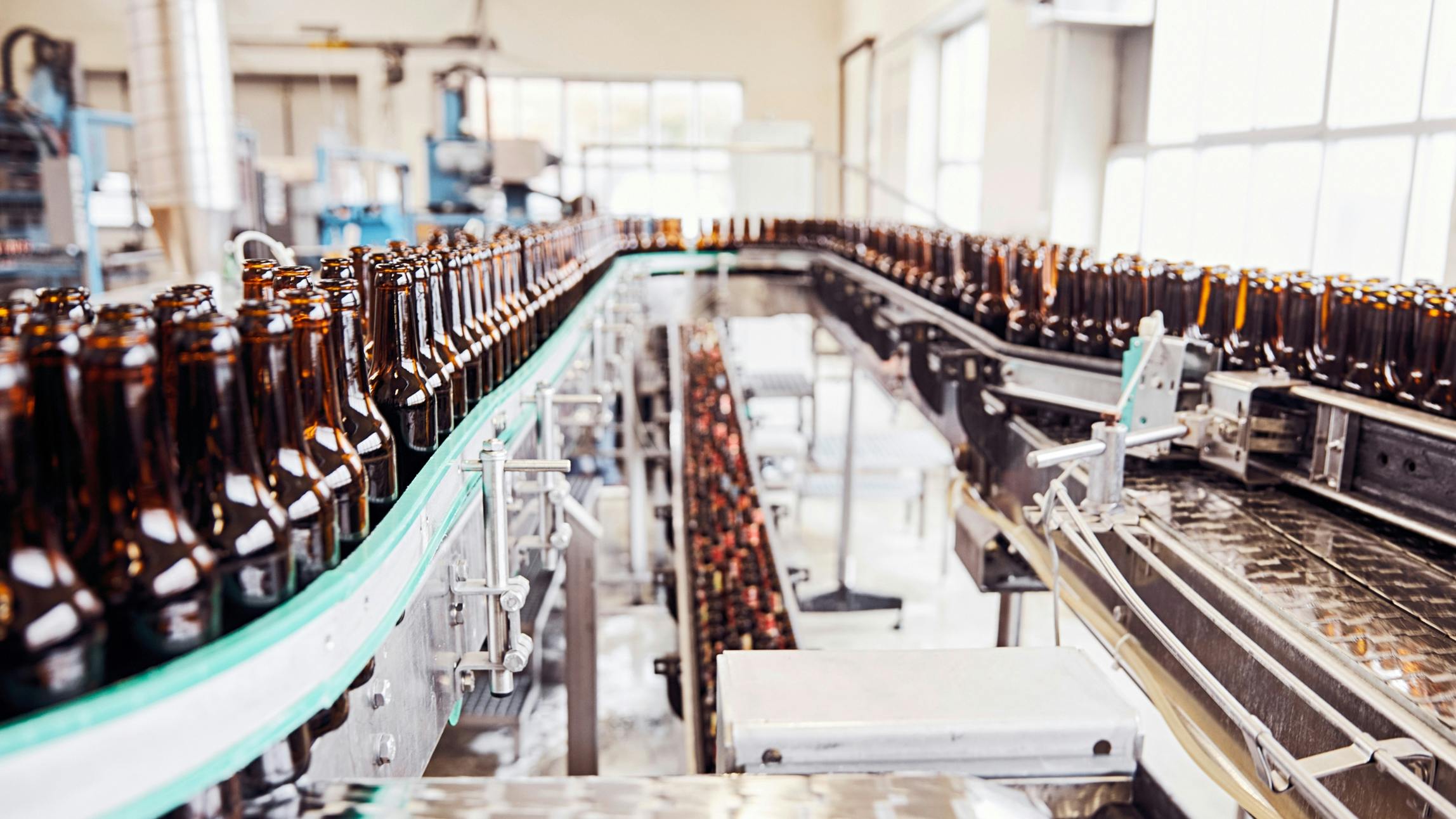 Ein Förderband in der Produktion mit leeren Bierflaschen. © gobiq