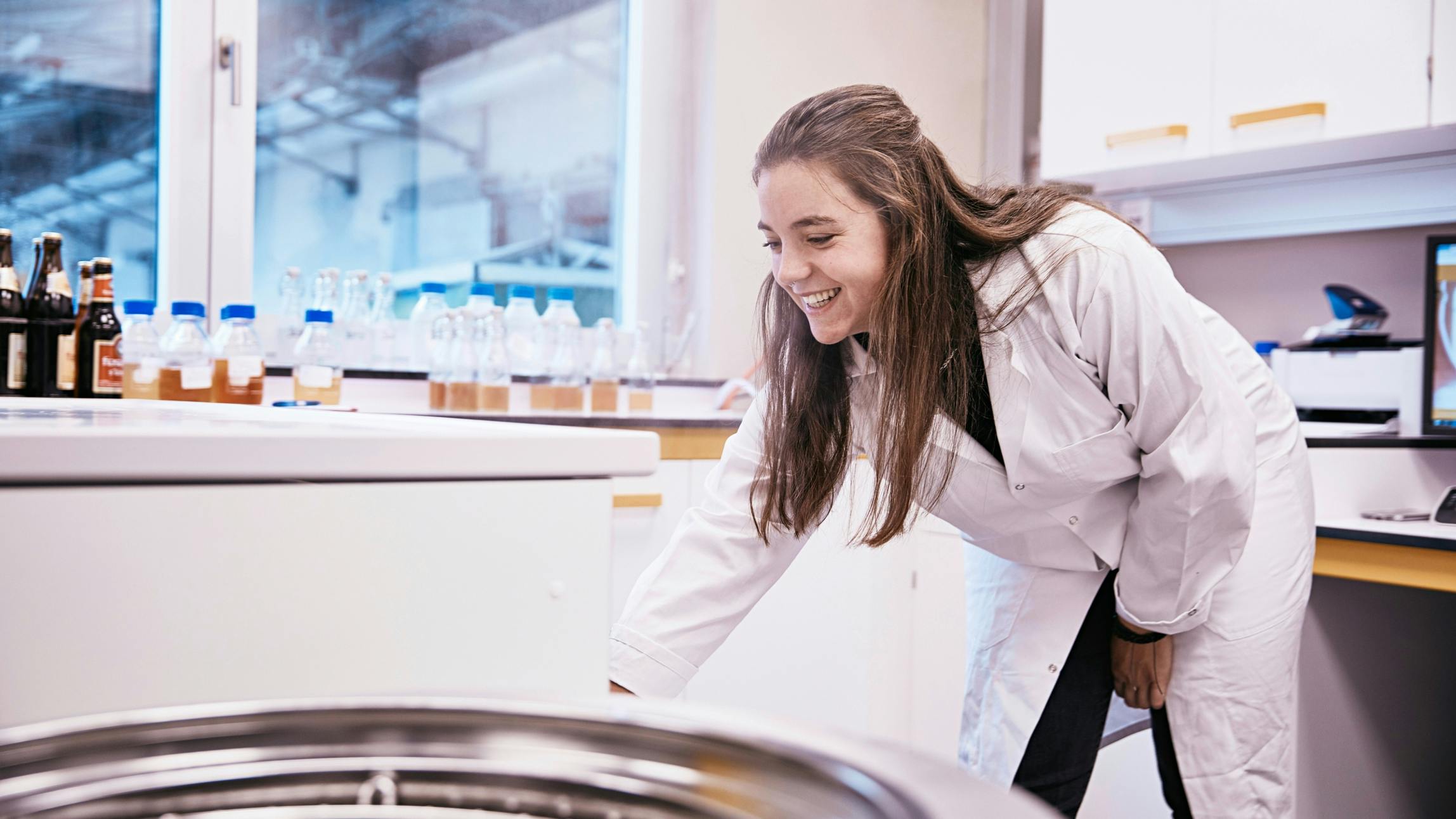 Eine Mitarbeiterin im Labor mit weißem Laborkittel lacht. © gobiq