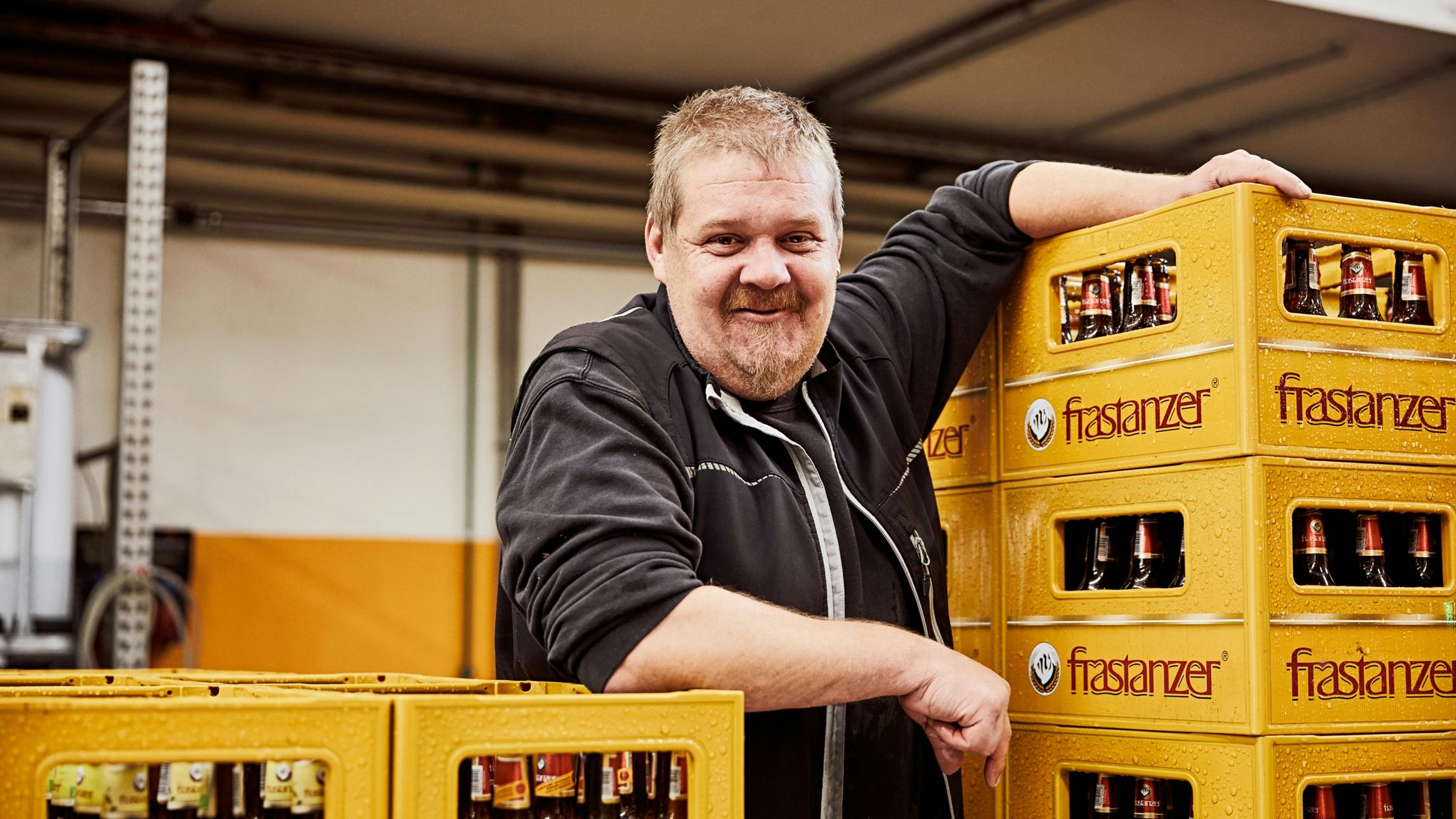 Ein Mitarbeiter der Frastanzer Brauerei neben mehreren gelben Frastanzer Bierkisten. © gobiq