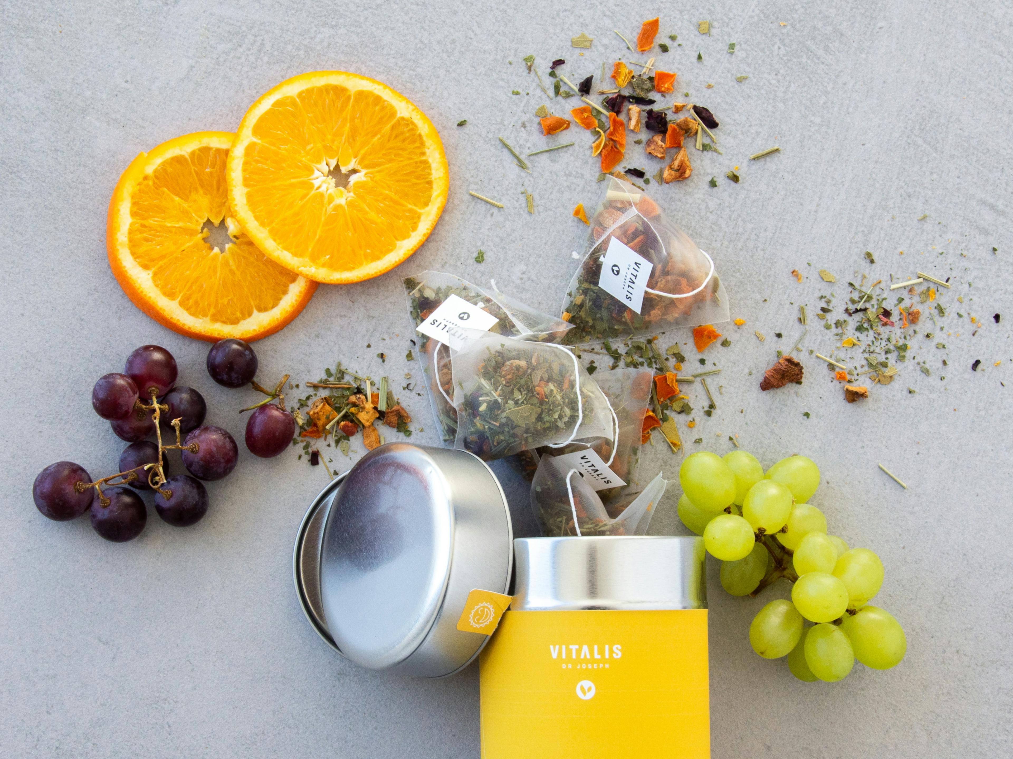 Produktfoto eines Vitalis Dr Joseph Tees platziert mit den enthaltenen Zutaten Orange und Traube © gobiq