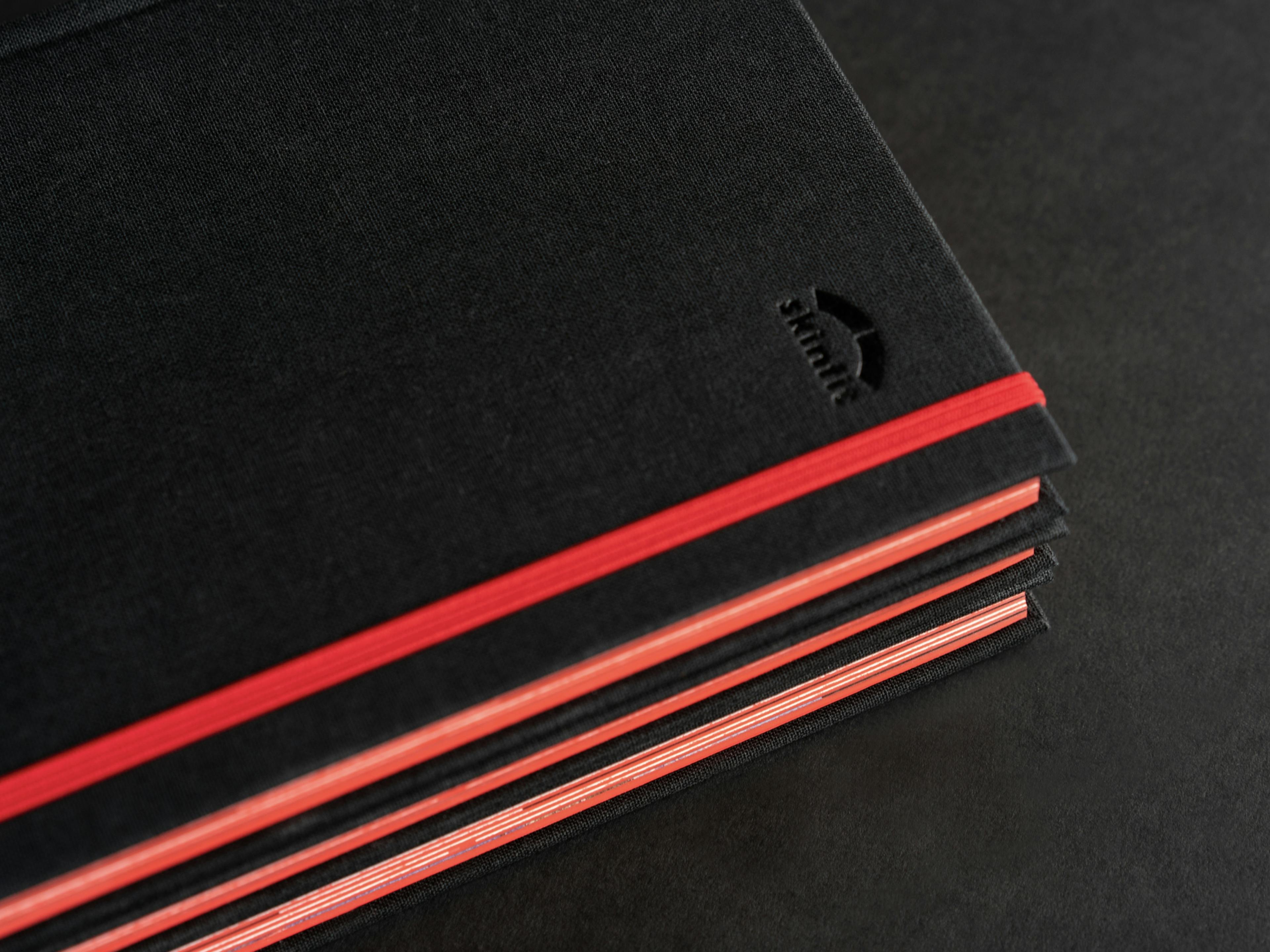 Detailfoto vom skinfit brandbook mit schwarzem Leineneinband, Blindprägung, rotem Gummiband und rotem Farbschnitt © gm gobiq