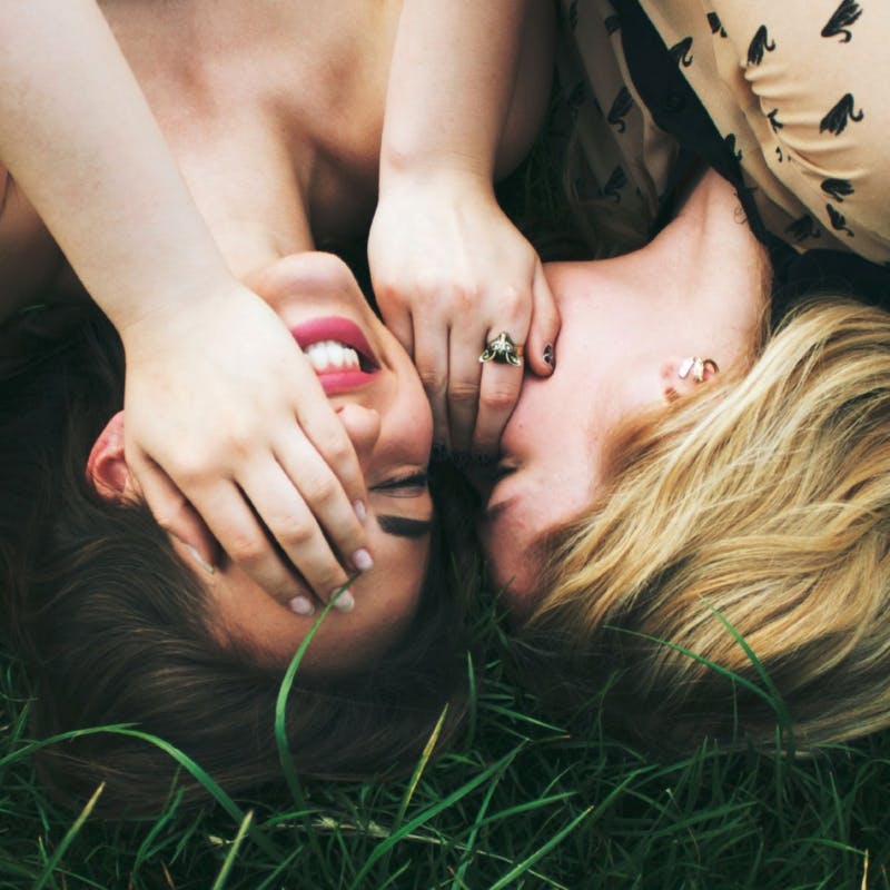 Zwei junge Frauen liegen in der Wiese und flüstern sich lachend etwas ins Ohr © gobiq
